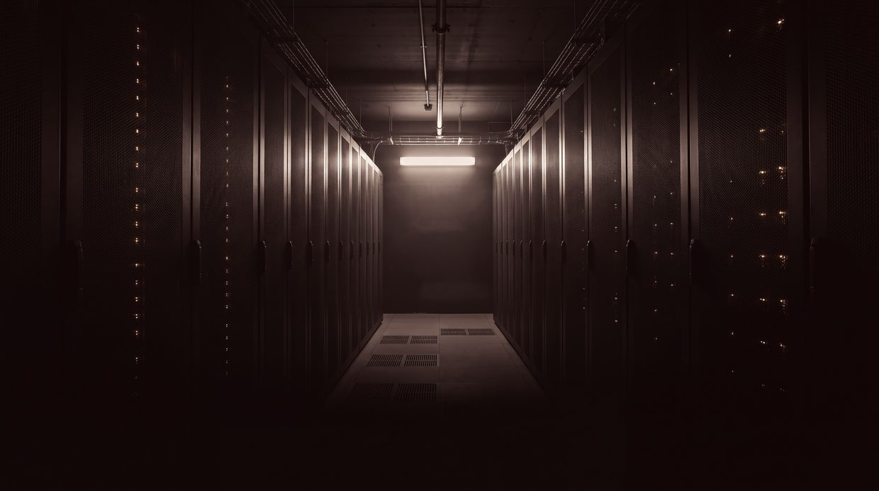Gång mellan serverskåp i en tom datorhall, upplyst nattetid av ett enda armaturljus. Ingen människa i rummet.